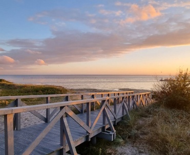 Drewniana kładka prowadząca przez wydmy w stronę zatoki zaprasza na wieczorny spacer po Jastarni. Pastelowe niebo i nadmorska roślinność budują spokojny klimat P&oacute;łwyspu Helskiego.
