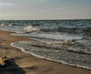Jasna, szeroka plaża z wydmami i wieżą w tle, uchwycona w słoneczny dzień przy czystym niebie.