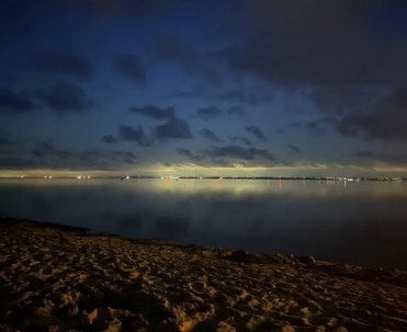 Ciemny, wieczorny kadr plaży z prześwitem światła nad horyzontem &ndash; bardziej nastrojowy niż poczt&oacute;wkowy.